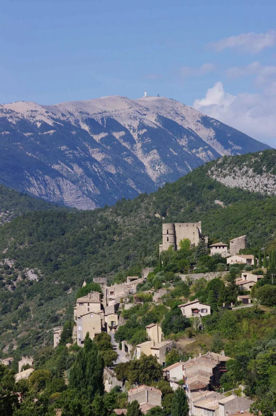 Village perché de Montbrun-les-Bains sur une colline verdoyante, avec le mont Ventoux en arrière-plan.