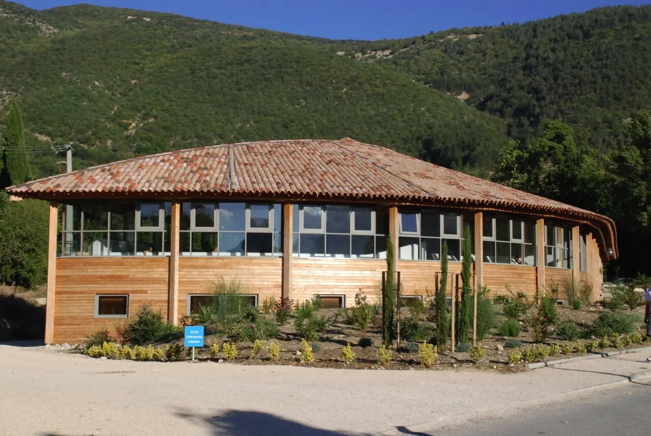 Bâtiment arrondi des thermes, habillé de bois et largement vitré, au pied d’une colline boisée.